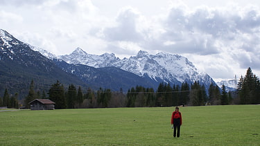 Hinter frühlingsgrünen Wiesen erhebt sich eine mächtige Gebirgskette.