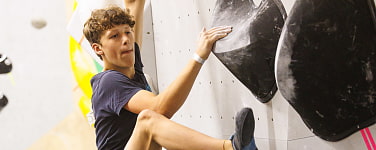 Bild zeigt eine beispielhafte Wettkampfszene: Ein Junge klettert an einer Boulderwand.