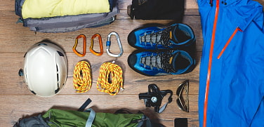 verschiedene Bergsteigerausrüstung von oben fotografiert. Bergschuhe, KLetterhelm, Regenjacke, Kletterseile und Karabiner 