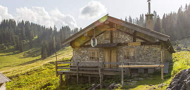 Bild der Bayrischen Wildalm, kleine Berghütte aus Stein & Holz im Morgenlicht am Berghang 