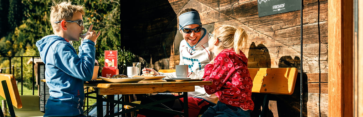 Frau mit zwei Kindern bei Jause vor der Hütte 