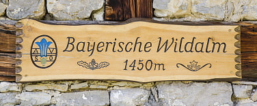 Holzschild mit der Aufschrift Bayerische Wildalm 1450m mit dem Enzian-Logo