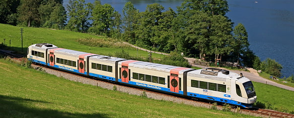 Bild zeigt den BOB Abkürzung für Bayerische Oberland Bahn wie sie entlang einem See fährt