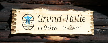 Holzschild mit der Aufschrift Gründ-Hütte 1195m mit dem Enzian-Logo
