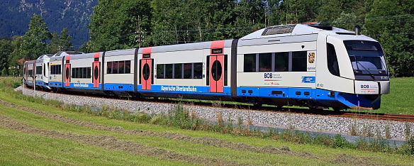 Bild zeigt den BOB Abkürzung für Bayerische Oberland Bahn wie er auf den Gleisen im Voralpenland fährt