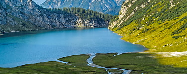 See mit Wiese und Felsenlandschaft