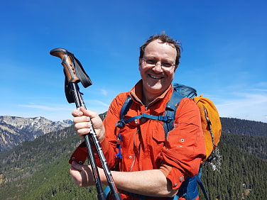 Berwanderer steht auf Gipfel mit weiteren Gipfeln im Hintergrund
