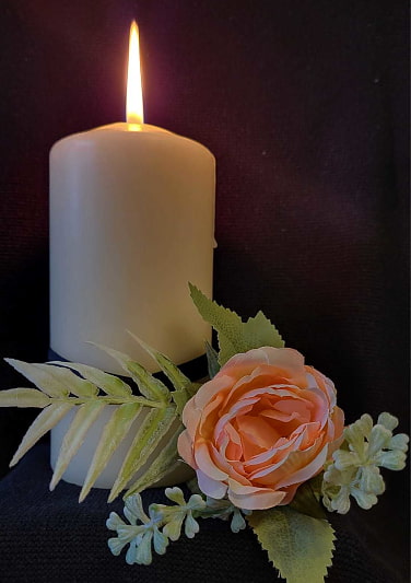 Eine weiße Kerze vor schwarzem Hintergrund mit rose farbener Rose.