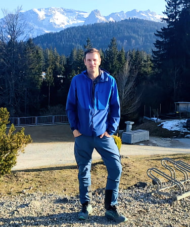 Michael Rix vor bewaldeten Hügeln und felsig verschneiten Bergen.