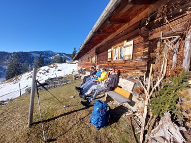 Die Gruppe macht Pause auf einer Bank hinterm Haus einer Alm. Auf dem Weg zum Seebergkopf.