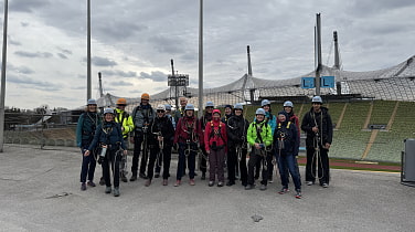 Eine große Gruppe mit Seil und Hüftgurten im Olympiastadion München kurz vor einer geführten Tour übers Zeltdach.