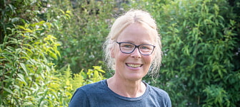 Bild zeigt ein Porträt von Alix von Melle. Sie hat blonde Haare zu einem Zopf zusammen gebunden und trägt eine dunkel gefaßte Brille und ein blaues T-Shirt
