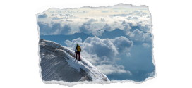 Bild zeigt einen Bergsteiger, der auf einem teilweise beschneiten Grad geht. Im Hintergrund die Berglandschaft gehült in Wolken
