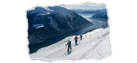 Bild zeigt drei Skitourengeher auf einer Route hoch über einem Tal eingerahmt von verschneiten Bergen