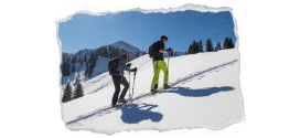 Bild zeigt eine weißen Hang mit Nadelbäumen im Hintergrund und 2 Schneeschuhwanderer in einer Spur nach oben