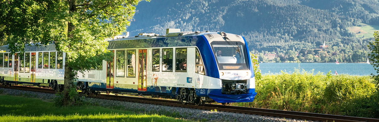 Bild zeigt den BOB Abkürzung für Bayerische Oberland Bahn in einer Großaufnahme wie er entlang einem Tegernsee fährt