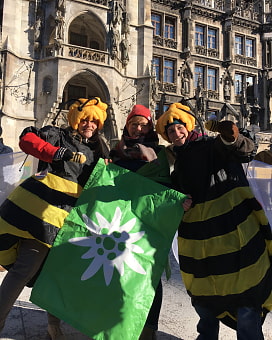Zwei als Biene verkleidete Menschen und eine weitere Person halten die Alpenvereinsflagge