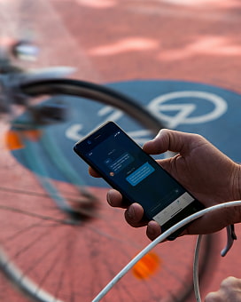 Verschwommenes Vorderrad und eine Hand, die ein Smartphone hält, die auf einem Lenker abgestützt ist.