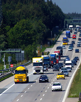 Sechsspurige Autobahn, die stark befahren ist. Viele LKWs und PKWs.