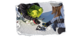 Bild zeigt zwei Skifahrer in der Hocke, die ein Lawinensuchgerät in der Hand halten