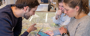 Drei Personen betrachten digitale und analoge Wanderkarte