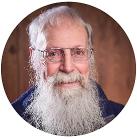 Auf dem Bild sieht man ein rundes Portrait von Dr. Walter Bien, Ausbildung & Touren. Er hat einen langen, weißen Bart und graue Haare. Er trägt ein Brille mit einem Metallgestell. Auf dem Bild trägt er einen dunkelblauen Pullover. Im Hintergrund erkennt man eine Holzvertäfelung.  