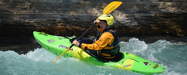Bild mit Wildwasserpaddler in bewegtem Fluss mit grünem Boot