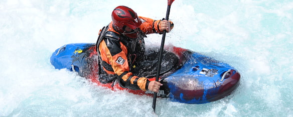 Ein Paddler auf Wildwasser. Wasser ist weiß aufgeschäumt.