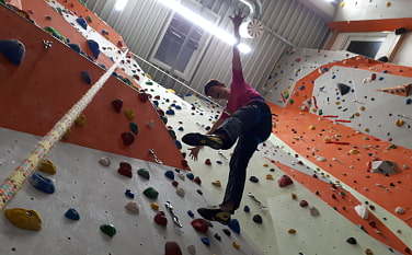 Kletterin in der Kletterhalle, die gerade am Seil hängt und von ihrem Kletterpartner gesichert wird.