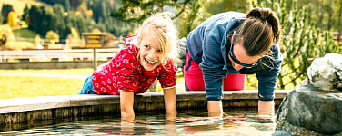 Frau und Kind halten ihre Hände in den Brunnen am Kneipbecken der Oberlandhütte