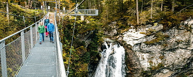 Kinder gehen über die Hängebrücke neben dem Wasserfall