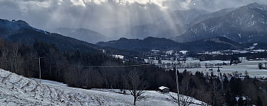 Ein schneebedeckter Hang mit Bergblick und die Sonne bricht durch die Wolkendecke