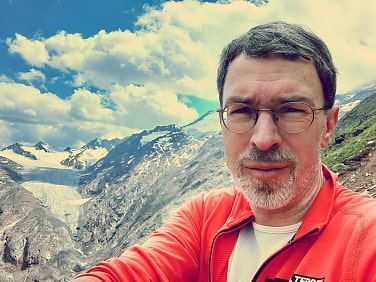 Matthias Heinze in roter Fließjacke vor einer Gebirgslandschaft.
