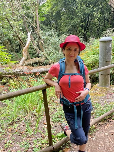 Paula lehnt sich entspannt an ein Holzgeländer. Hinter ihr ist Wald.