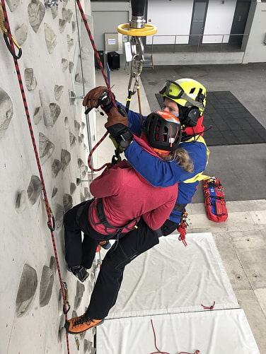 Bergwachtkler schneide verletzte Person an Kletterwand aus Seil.