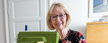 Ältere Frau sitzt an ihrer Nähmaschine und lächelt