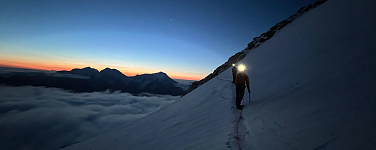 Person mit Stirnlampe in der Morgendämmerung am Berg