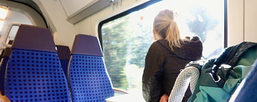 Frau mit Rucksack sitzt in einer Bahn und schaut zum Fenster hinaus. 