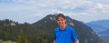Mann in blauem Poloshirt steht vor einem Bergpanorama