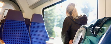 Frau sitzt in Bahn und schaut aus dem Fenster Ein Wanderrucksack steht auf dem Sitz neben ihr.