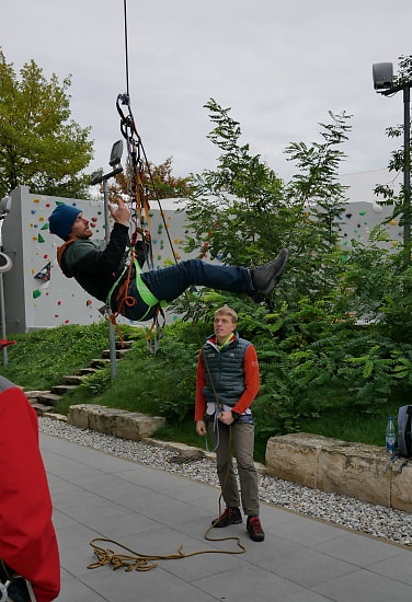 Mensch hängt in Kletterhalle in Klettergurt und baut einen Seilzug.