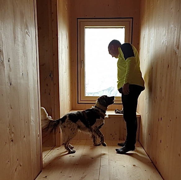 Hund und Mensch stehen in einem Raum der mit Holz vertäfelt ist.