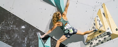 Frau mit Pferdeschwanz hängt mit einer Hand an einem Boulder. 