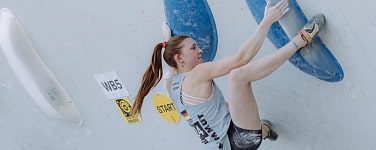Mensch klettert im Lead an einer leicht überhängenden Kletterwand mit Kunstgriffen