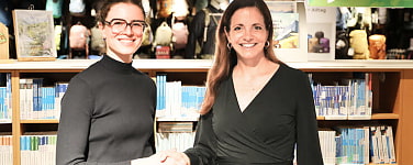 Zwei Frauen geben sich die Hand und lächeln in die Kamera.