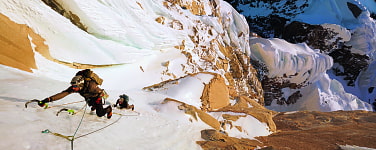 Menschen klettern mit Eisgeräten eine steile, schneebedeckte Rinne empor.