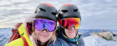 Mann und Frau lächeln in Kamera. Beide tragen Skihelme und Skibrillen.