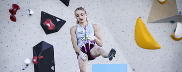 Kletterin (Anna Apel) sitzt hängend im Klettergurt und blickt nach unten