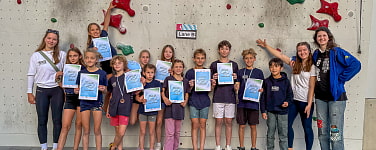 Gruppe von Kindern vor Kletterwand. Viele halten eine Urkunde in die Kamera.